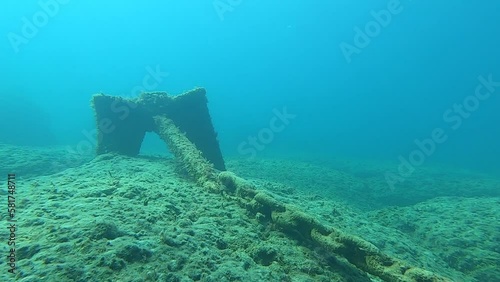 Anchor chain and anchor on the seabed. An anchor chain covered with algae stretches along the rock bottom. photo