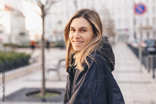 Happy blonde woman wear navy blue bomber jacket walking in the street and smiling to camera. Stylish girl in fashion outfit walking over the city. What a beautiful day out. Girl turn around.