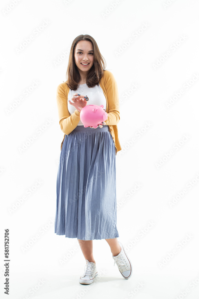 A woman puts a coin in a piggy bank on a white background. Happy model collects for a long-awaited purchase A woman puts a coin in a piggy bank on a white background. Happy model collects for a long-awaited purchase