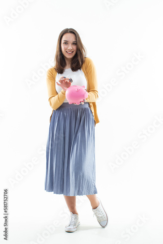 A woman puts a coin in a piggy bank on a white background. Happy model collects for a long-awaited purchase