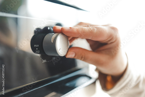 Women in modern kitchen turning on oven. Close up view of female hand and oven button