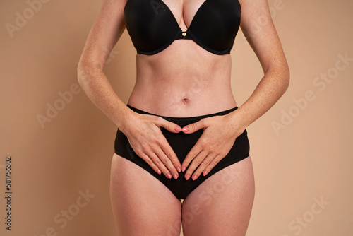 Unrecognizable woman in black underwear keeping hands on her abdomen