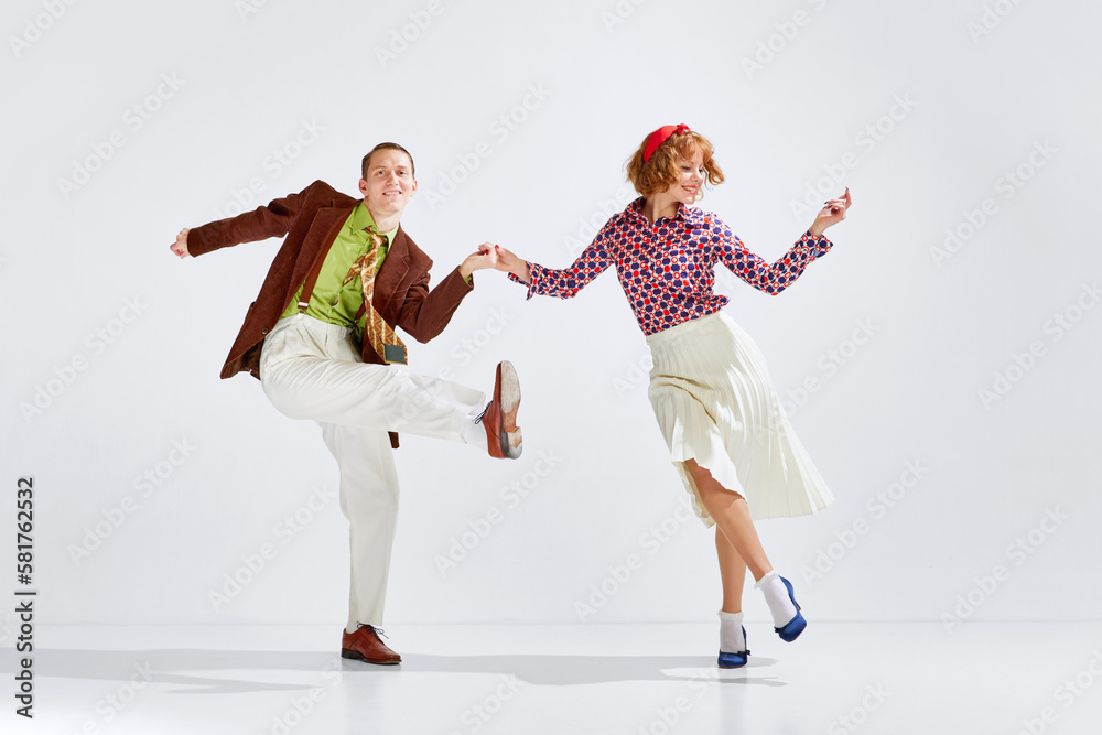 Feeling happy and positive. Young smiling man and woman in stylish clothes dancing retro dance against grey studio background. Concept of art, retro style, hobby, party, movements, 60s, 70s culture