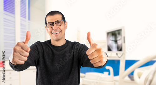 Man wearing casual sweater and glasses at consulting room.Success sign doing positive gesture with hand, thumbs up smiling and happy. Cheerful expression and winner photo