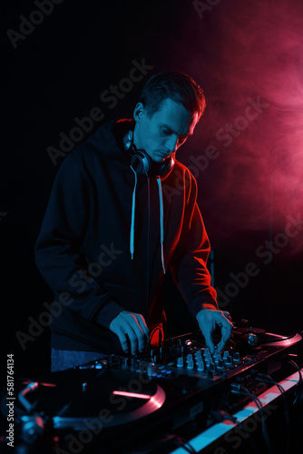 Cool young DJ playing vinyls on party. Disk jokey mixing musical tracks in dark night club