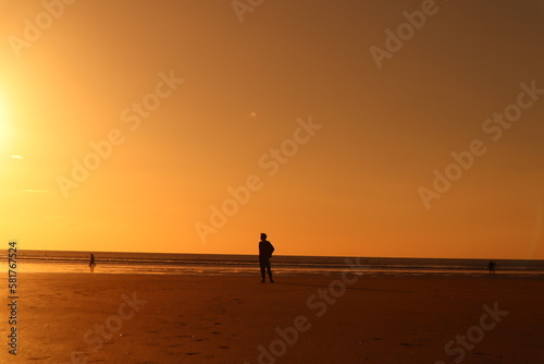 Ambient orange sunset on beach with silhouette of man