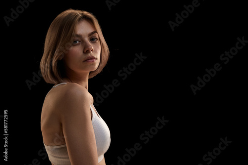 Young slim sensual woman wearing white bra looking at caemra over dark background. Concept of dieting, healthy lifestyle, natural beauty, body and skin care