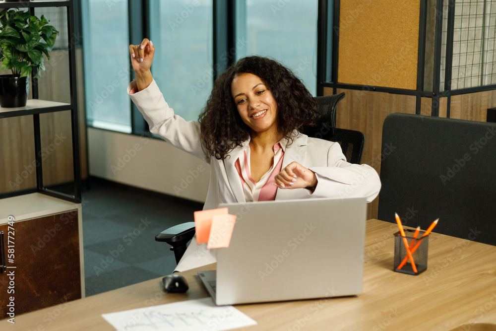 © AvokadoStudio - Young Successful African American Project Manager Dances and Smiles While Sitting at Her Desk