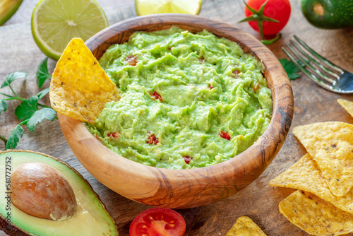 Guacamole, guacamole ingredients and chips on wooden background.