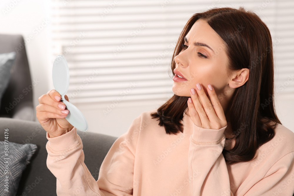 Young woman looking in mirror and touching her face indoors. Hormonal disorders Young woman looking in mirror and touching her face indoors. Hormonal disorders