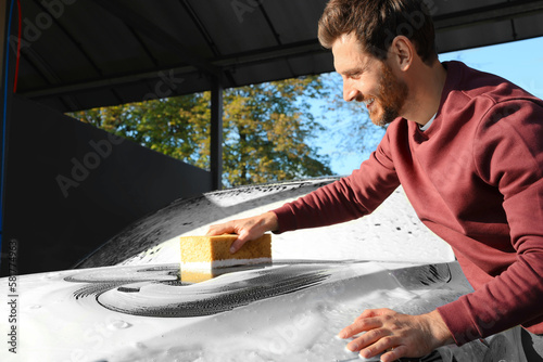 Worker washing auto with sponge at outdoor car wash