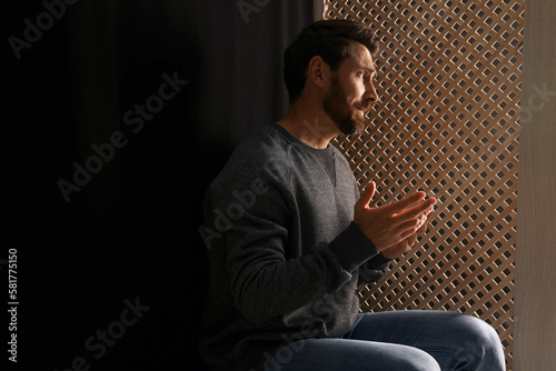 Man listening to priest during confession in booth, space for text photo