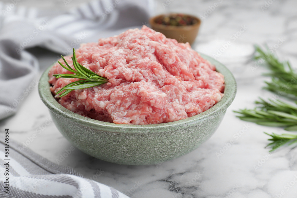Bowl of raw fresh minced meat with rosemary on white marble tabl Bowl of raw fresh minced meat with rosemary on white marble tabl