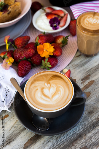 flat white coffee with loveheart latte art, on a cafe table with dessert and strawberries photo