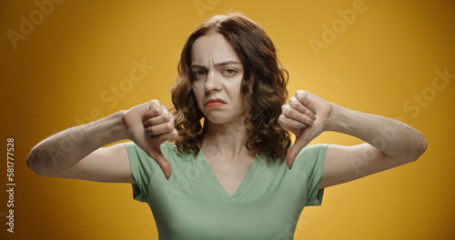 Tableau sur toile Pale caucasian girl looking at camera and gesturing negative sign of thumbs down, isolated on yellow background