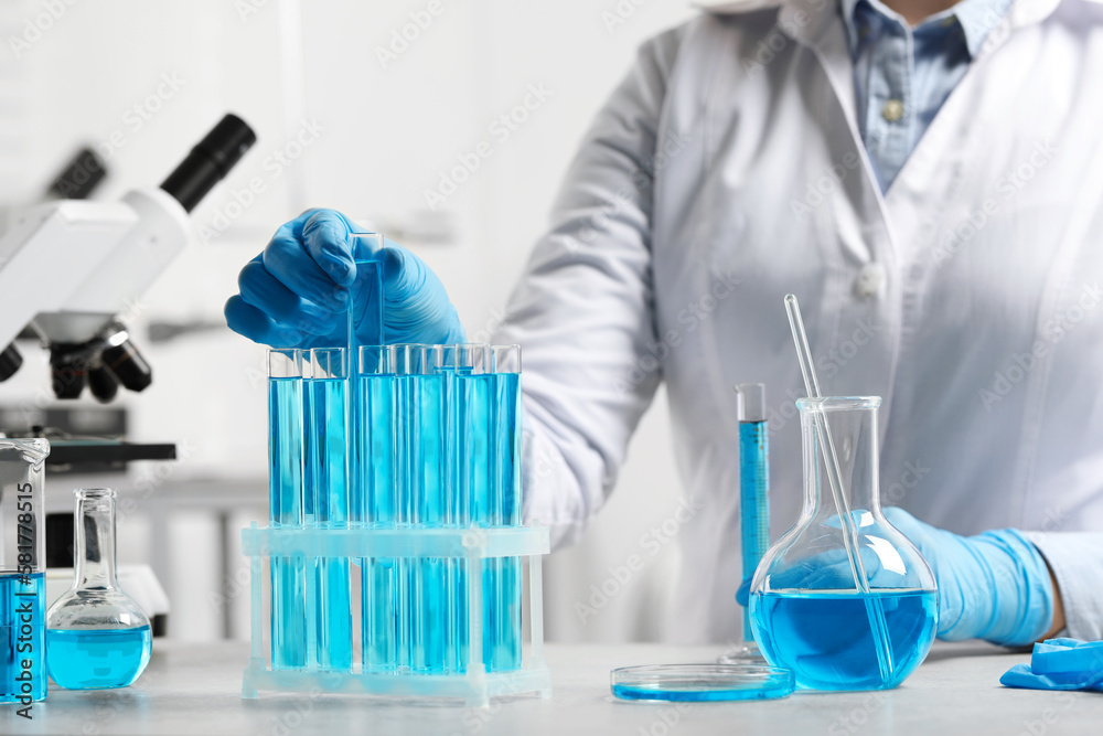 Scientist dripping liquid from pipette into test tube at white table in laboratory, closeup Scientist dripping liquid from pipette into test tube at white table in laboratory, closeup