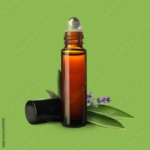 Bottle of lavender sage essential oil, leaves and flowers on light green background