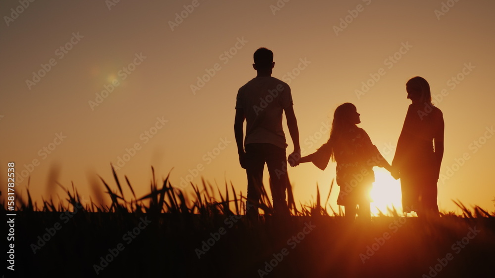 A happy family of three people meets the dawn in a picturesque place. Holding hands