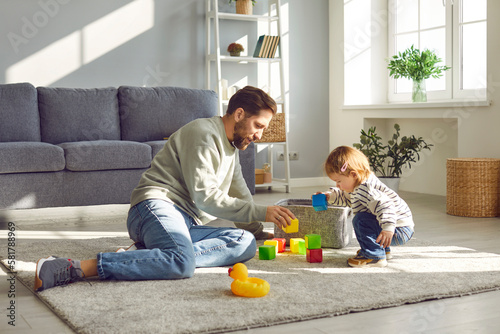 Parenthood. Loving young father with his toddler daughter playing with colored blocks at home. Caucasian father sitting on floor in living room enjoy leisure weekend together with his small child.