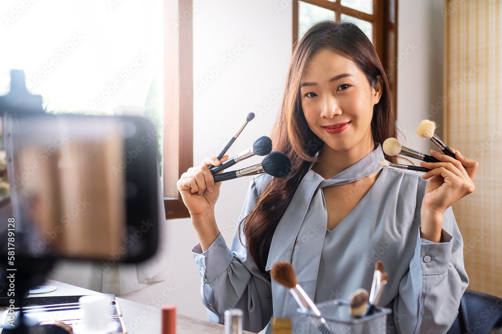 Young beauty blogger asian girl poses with holding make up brush on mobile live cam