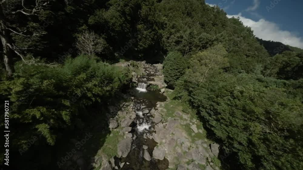 FPV aerial of small waterfall and stream through green Azores forest FPV aerial of small waterfall and stream through green Azores forest