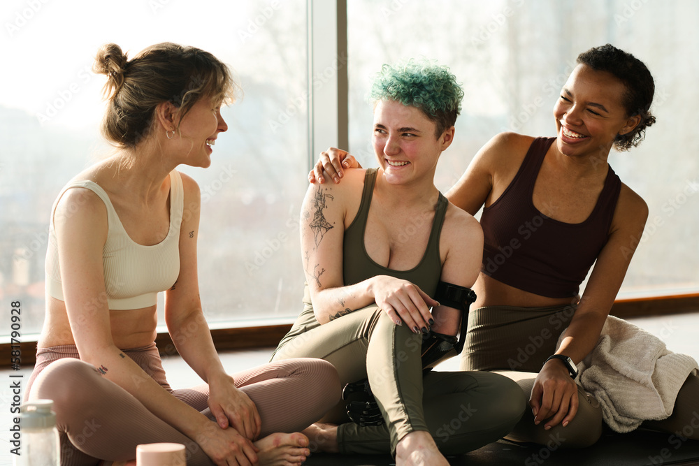 Obraz premium Group of happy girls talking to each other and smiling after sport training in gym