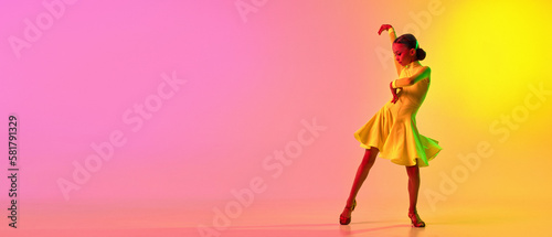 Fotografija Elegant little girl in adorable stage outfit, dress dancing ballroom dance over gradient pink-yellow background in neon light filter