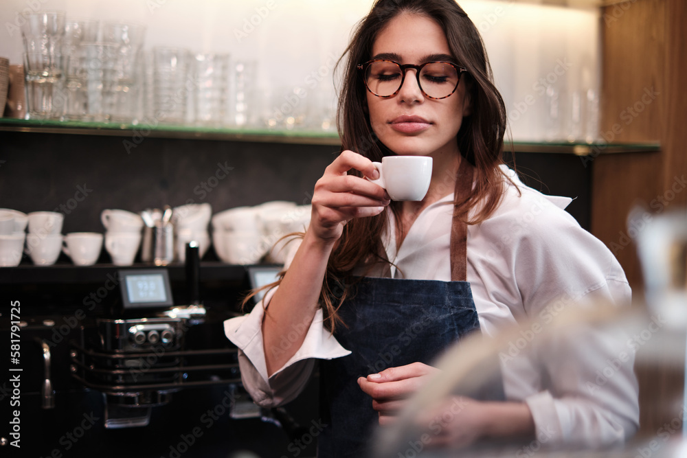 Portrait of a waitress standing at coffee shop and trying out coffee. - obrazy, fototapety, plakaty 