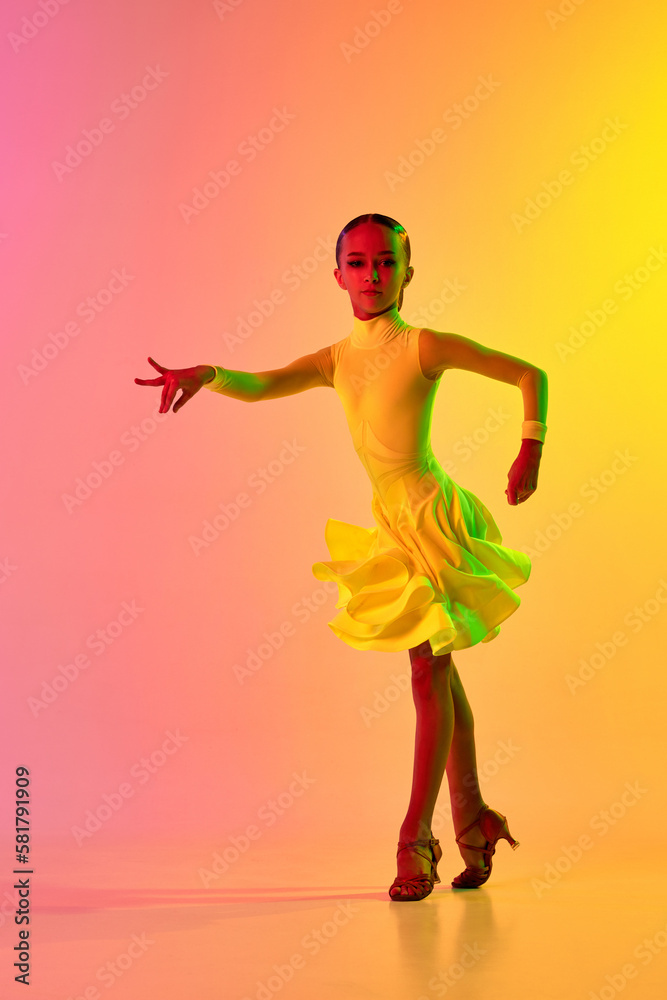 Expressive little girl in adorable stage outfit, dress dancing ballroom dance over gradient pink-yellow background in neon light filter. Concept of beauty, professional dances, skills