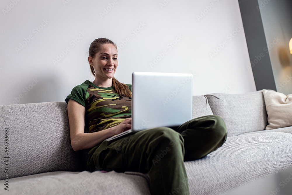 Female soldier making video call using laptop at home while sitting on sofa. Female soldier making video call using laptop at home while sitting on sofa.