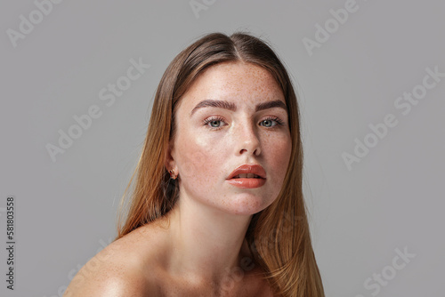 Studio beauty portrait of very natural woman with freckles on her face. Girl looking at the camera.