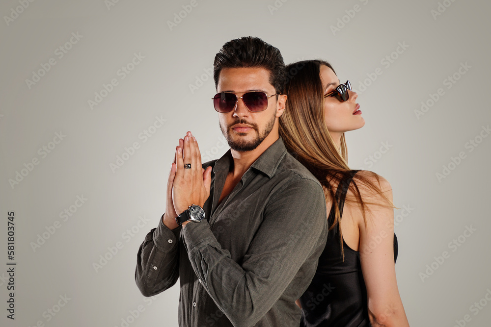 Fashion photo of handsome young couple posing together in studio, wearing summer sunglasses.