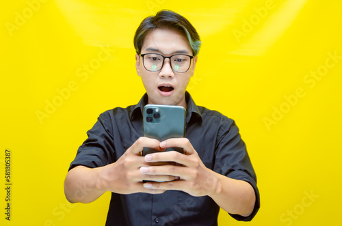 Slika na platnu overjoyed young asian man with peek a boo colored hair wearing black shirt holding phone