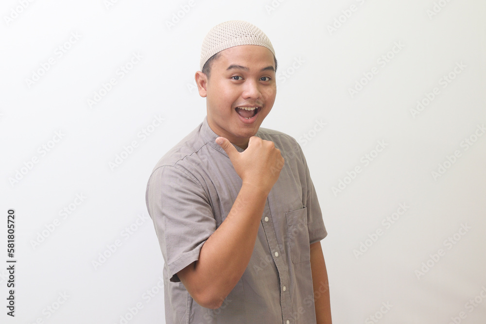 Portrait of a smiling young Asian Muslim, thumb pointing sideways. Isolated image on a white background Portrait of a smiling young Asian Muslim, thumb pointing sideways. Isolated image on a white background