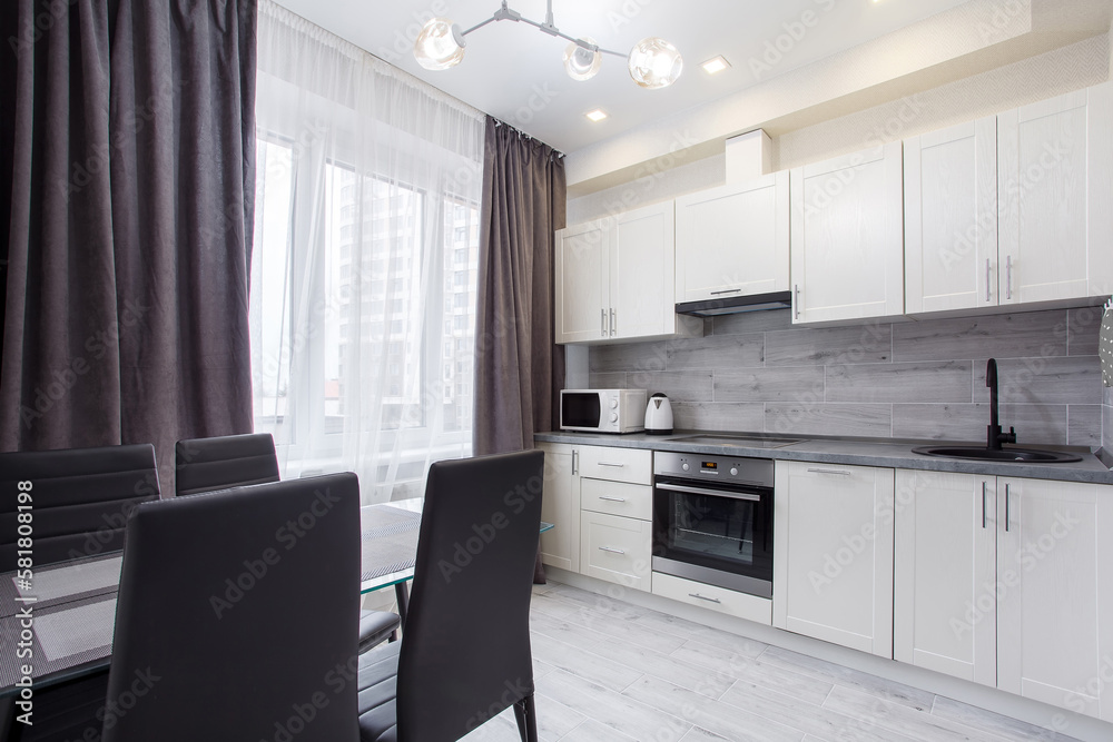 Clean kitchen in a small cozy contemporary studio apartment. Table and chairs in the foreground. Built in household appliance Clean kitchen in a small cozy contemporary studio apartment. Table and chairs in the foreground. Built in household appliance