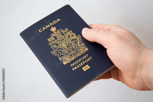 Hand of a white woman holding a Canadian passport in front of a white background with natural light photo