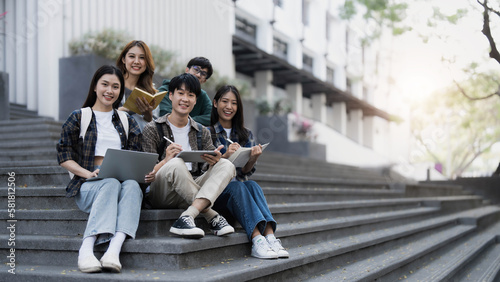 Group of cheerful Asian college students sitting on stairs, showing fists, celebrating triumph