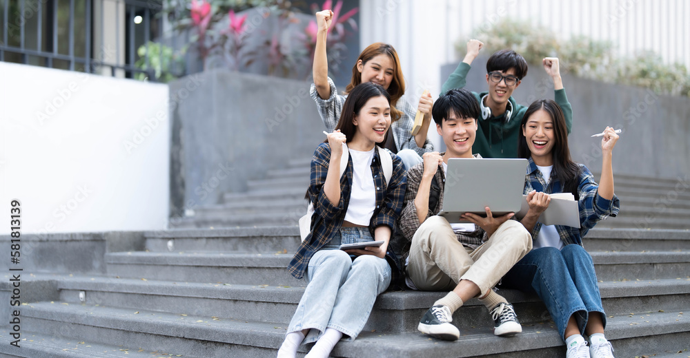 Obraz premium Group of cheerful Asian college students sitting on stairs, showing fists, celebrating triumph