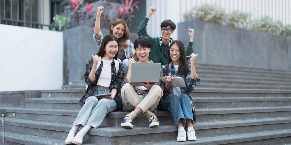 Obraz premium Group of cheerful Asian college students sitting on stairs, showing fists, celebrating triumph