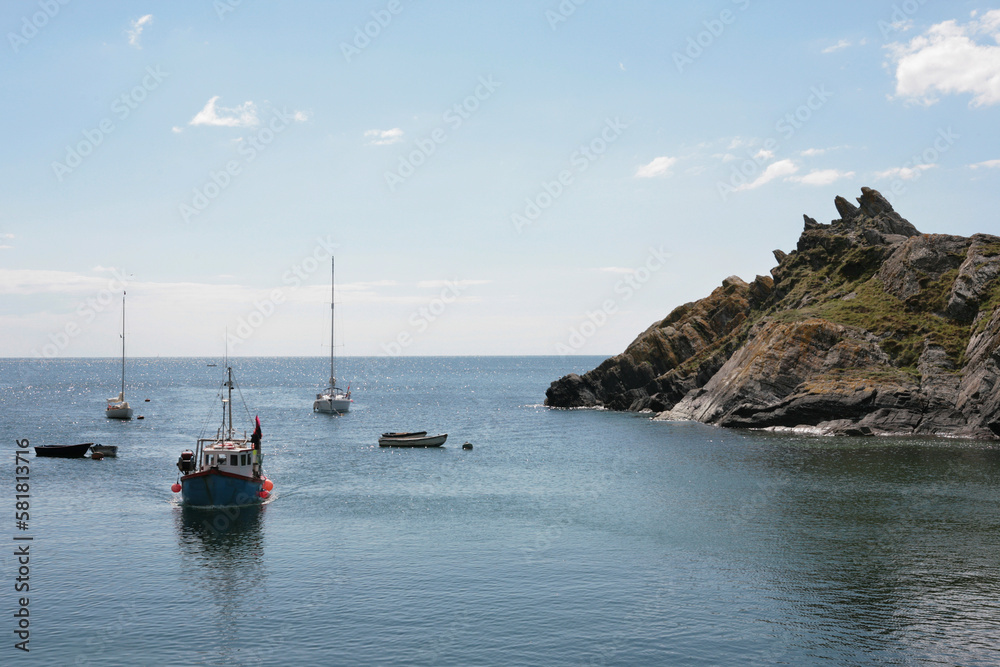 A local fishing boat approaching the entrance to Polperro harbour, Cornwall, UK, with other yachts moored in the outer harbour