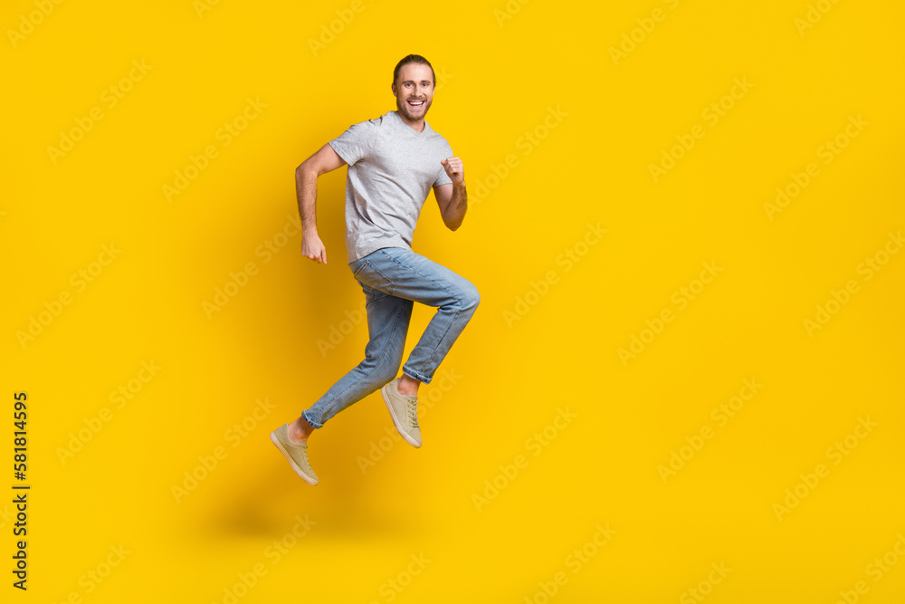 Full length photo of excited funky guy dressed grey t-shirt jumping high running fast empty space isolated yellow color background