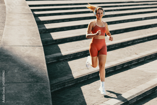 Fototapeta Naklejka Na Ścianę i Meble -  Athletic female using music to enhance running and jogging outdoor stairs workout