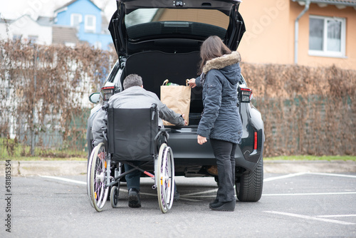 A woman helps a disabled person on a wheelchair to pack groceries into the car © Natalje Dietrich