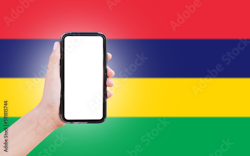 Male hand holding smartphone with blank on screen, on background of blurred flag of Mauritius. Close-up view.