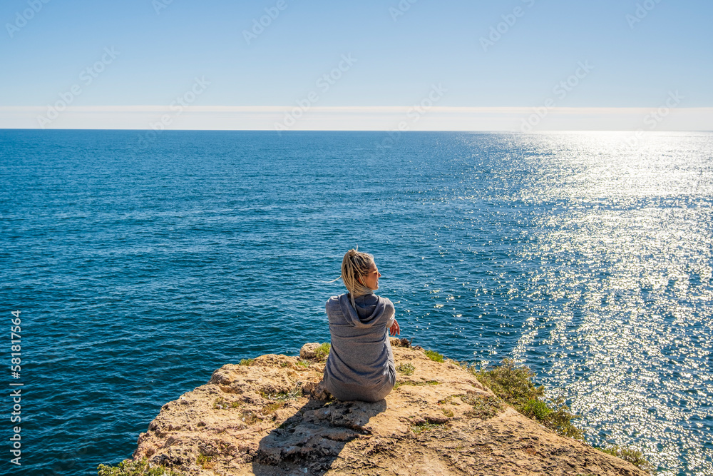 A woman enjoying the ocean view from the top of cliffs at Marinha Beach in Algarve, Portugal