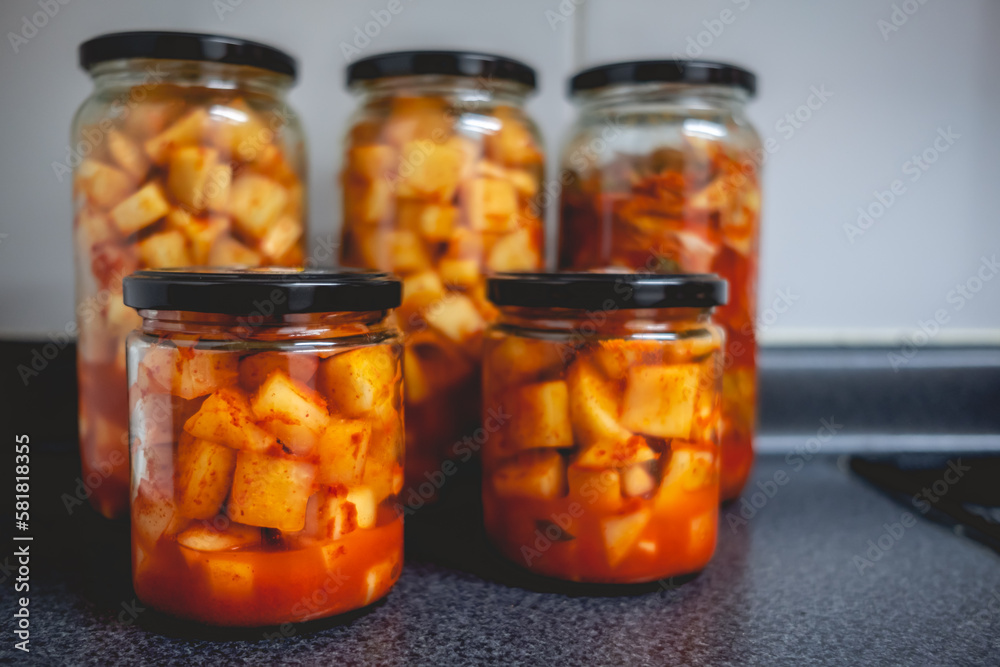 Details of spicy traditional kimchi in glass jars in kitchen (kimchi: mix of pickled and fermented vegetables like turnip or lettuce, garlic, chili peppers, salt) Details of spicy traditional kimchi in glass jars in kitchen (kimchi: mix of pickled and fermented vegetables like turnip or lettuce, garlic, chili peppers, salt)