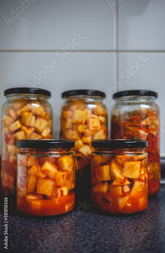 Details of spicy traditional kimchi in glass jars in kitchen (kimchi: mix of pickled and fermented vegetables like turnip or lettuce, garlic, chili peppers, salt)