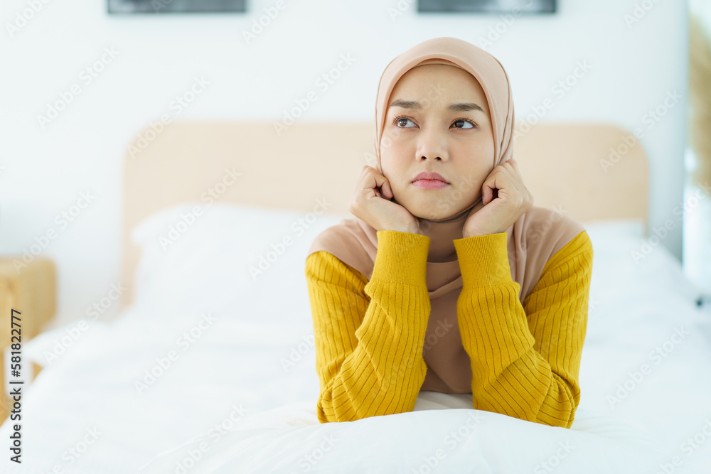 Unhappy - stressful Asian young muslim woman sitting alone on the bed in the morning. Asian muslim woman having a mental burn out or depression problem from working and social environment. Unhappy - stressful Asian young muslim woman sitting alone on the bed in the morning. Asian muslim woman having a mental burn out or depression problem from working and social environment.