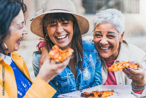 Women eating pizza outdoors at city - Happy three senior having fun together outside on street and laughing with food- Friendship and lifestyle concept