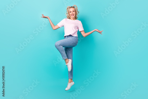 Full length photo of positive pleasant girl wear striped t-shirt jumping demonstrate products isolated on vivid turquoise color background © deagreez